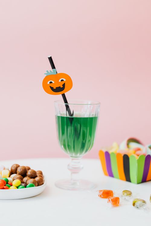 Free Festive Halloween green drink with a pumpkin-decorated straw, surrounded by colorful candies on a pink backdrop. Stock Photo
