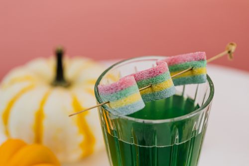 Free A colorful cocktail garnished with rainbow candy beside decorative pumpkins. Stock Photo