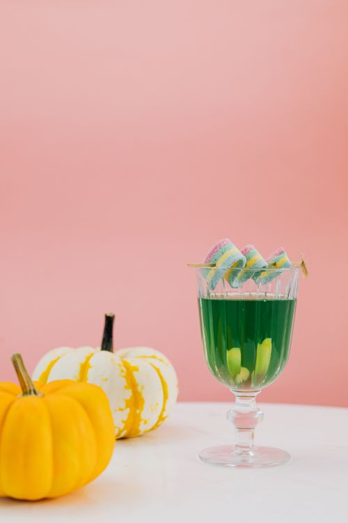 Free Vibrant green drink garnished with candies next to yellow pumpkins on a pink background. Stock Photo