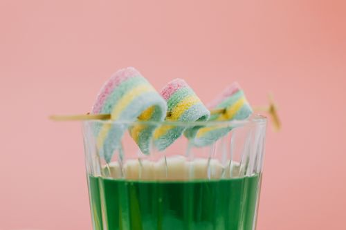 Free Colorful candy skewers dipped in green beverage against pink backdrop. Stock Photo