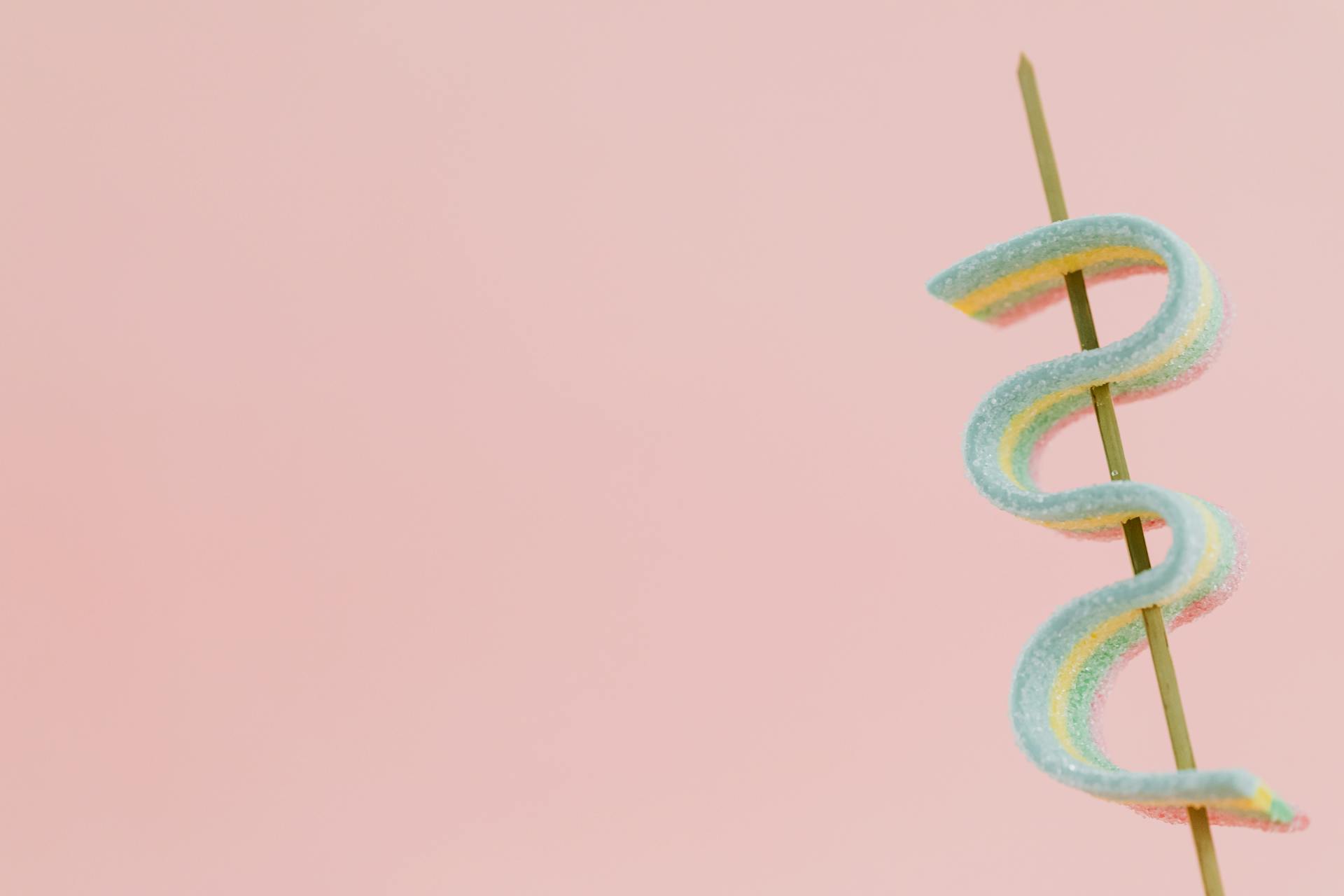 Bright and vibrant candy spiraled on a stick against a pink backdrop, offering ample copy space.