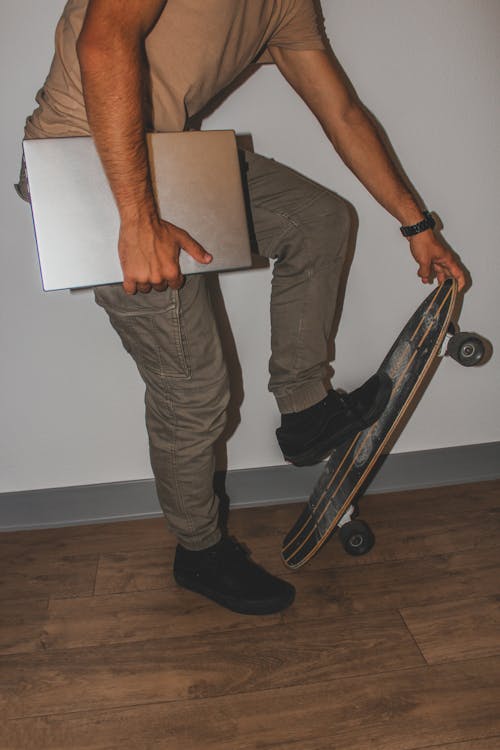 Man Holding a Laptop and a Skateboard 