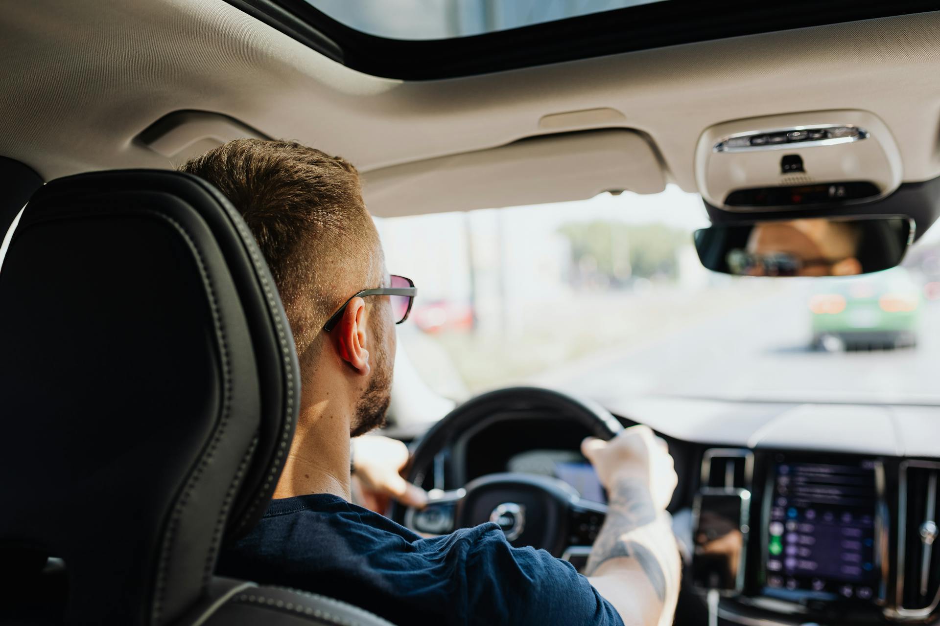 Rear view of a man driving a car with focus on interior details and steering.