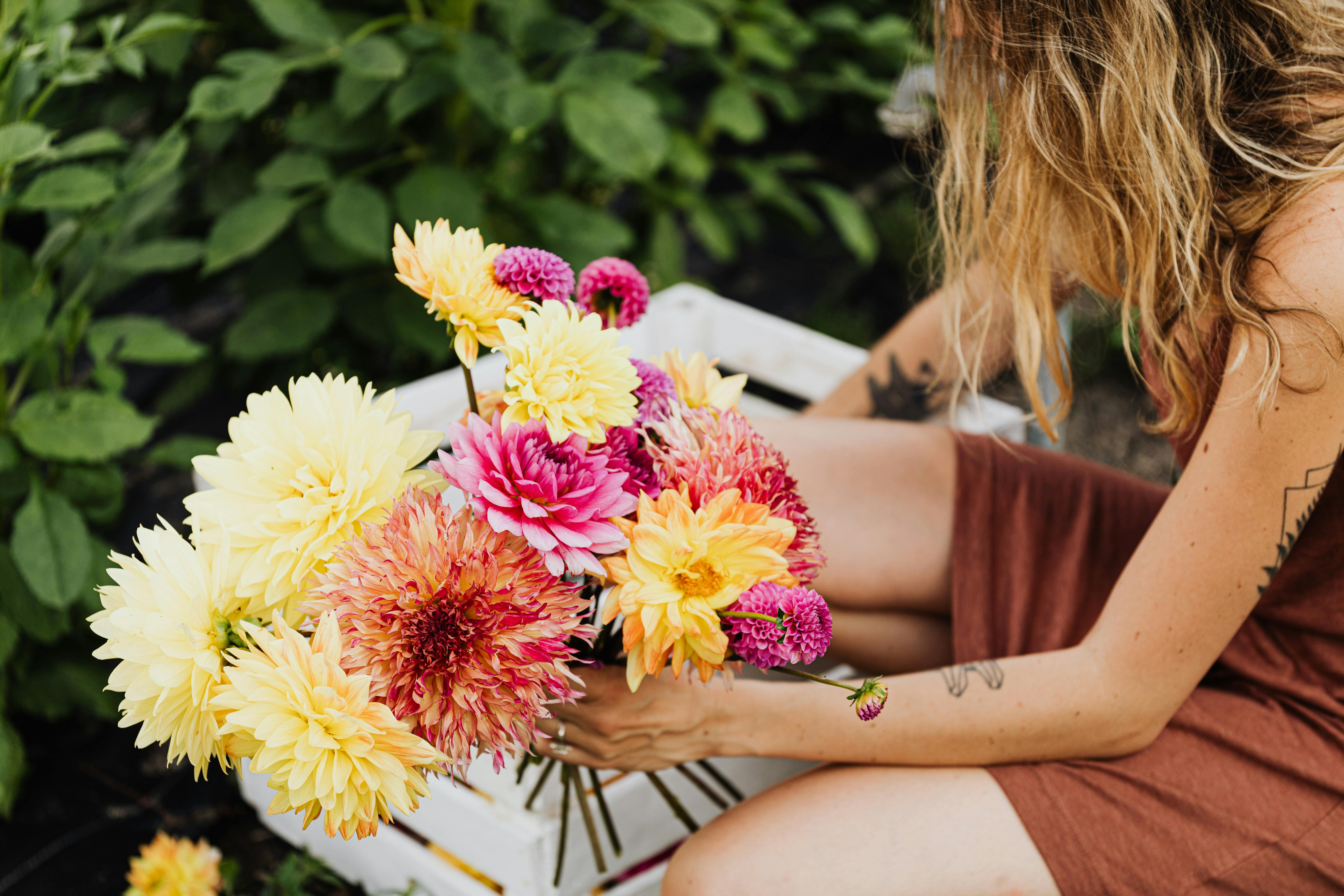 A woman in a dress holds a vibrant bouquet of dahlias outdoors, showcasing nature's beauty.