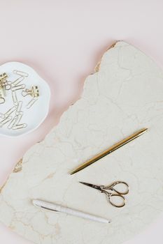Flat lay of gold pen, scissors, and clips on marble.