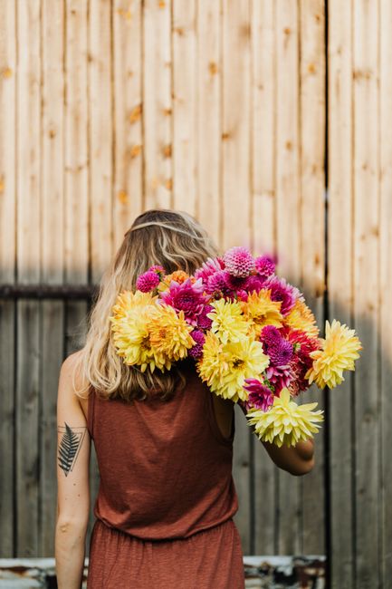 Back view of woman with colorful bouquet against rustic wooden wall showcasing natural beauty.