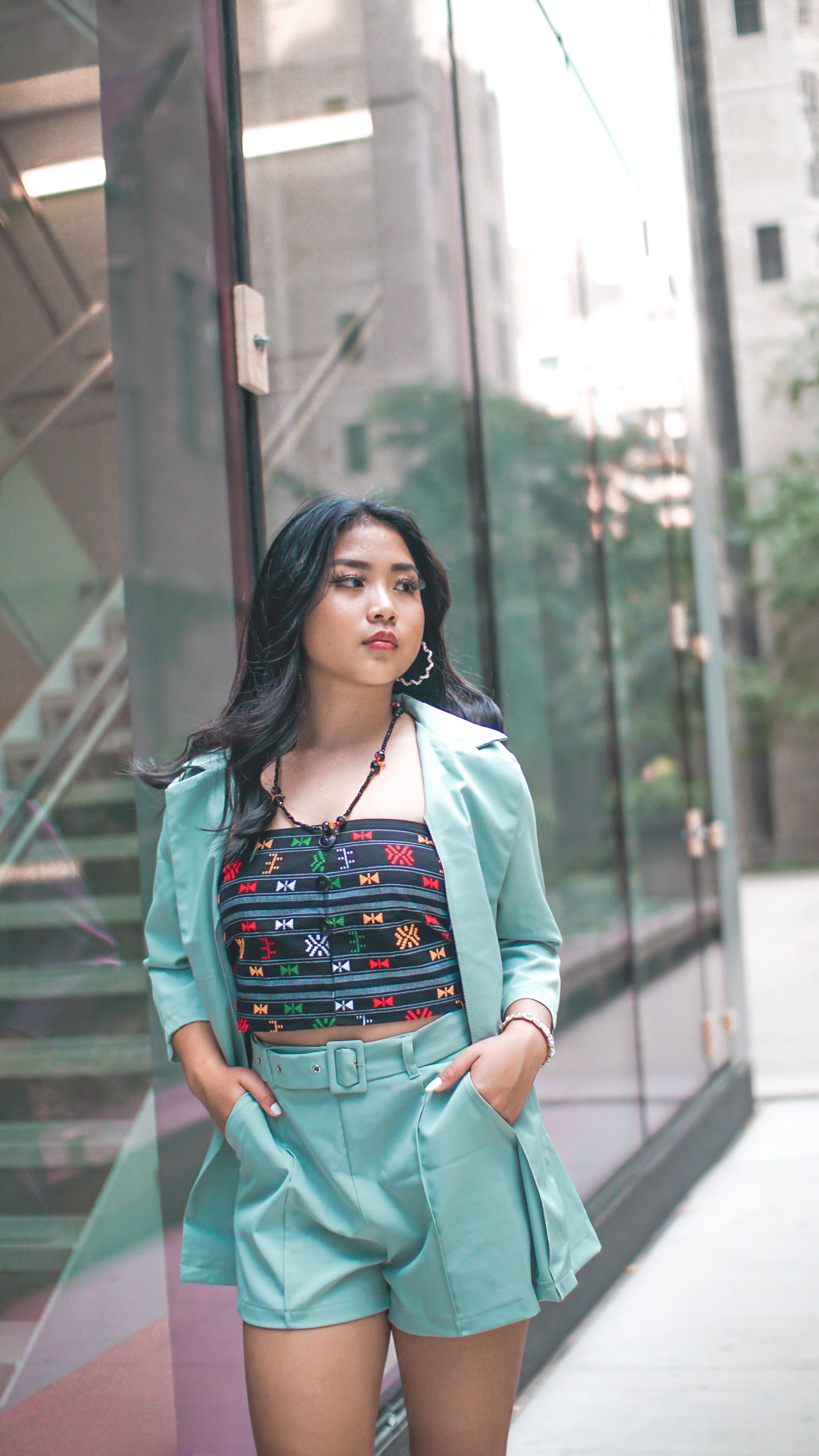 Confident woman posing in a chic outfit against glass buildings, creating a modern urban vibe.