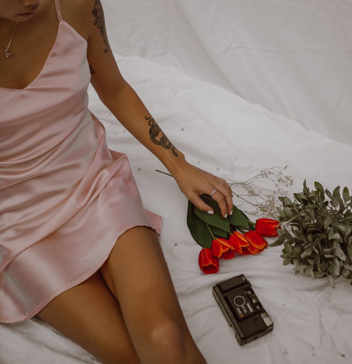 Free Crop alluring woman sitting on bed with flowers and retro photo camera Stock Photo