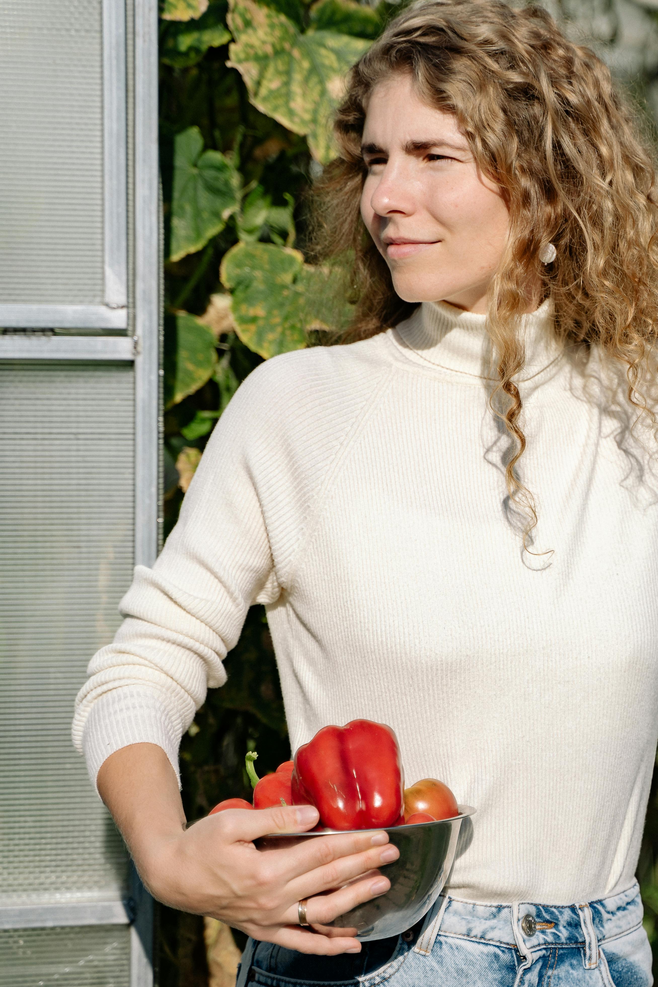 close up shot of a woman in white long sleeves holding a bowl of fruits