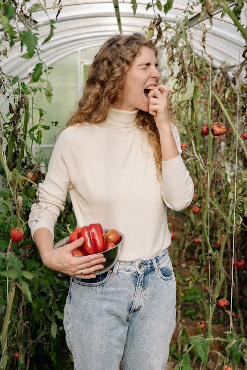 Woman in a Beige Turtleneck Sweater eating a Raw Vegetable 