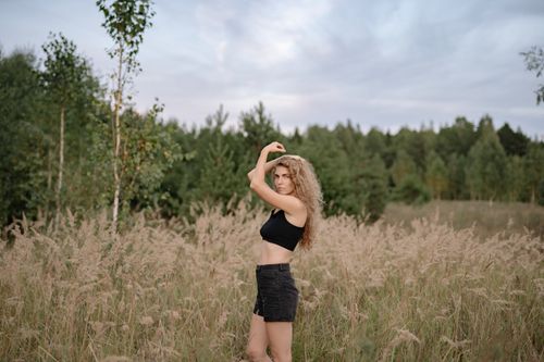Free A woman in a crop top and shorts poses in a grassy field, surrounded by trees and nature. Stock Photo