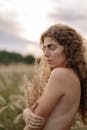 日落时分，一位卷发女子在草地上拥抱自然，构成一幅宁静的肖像