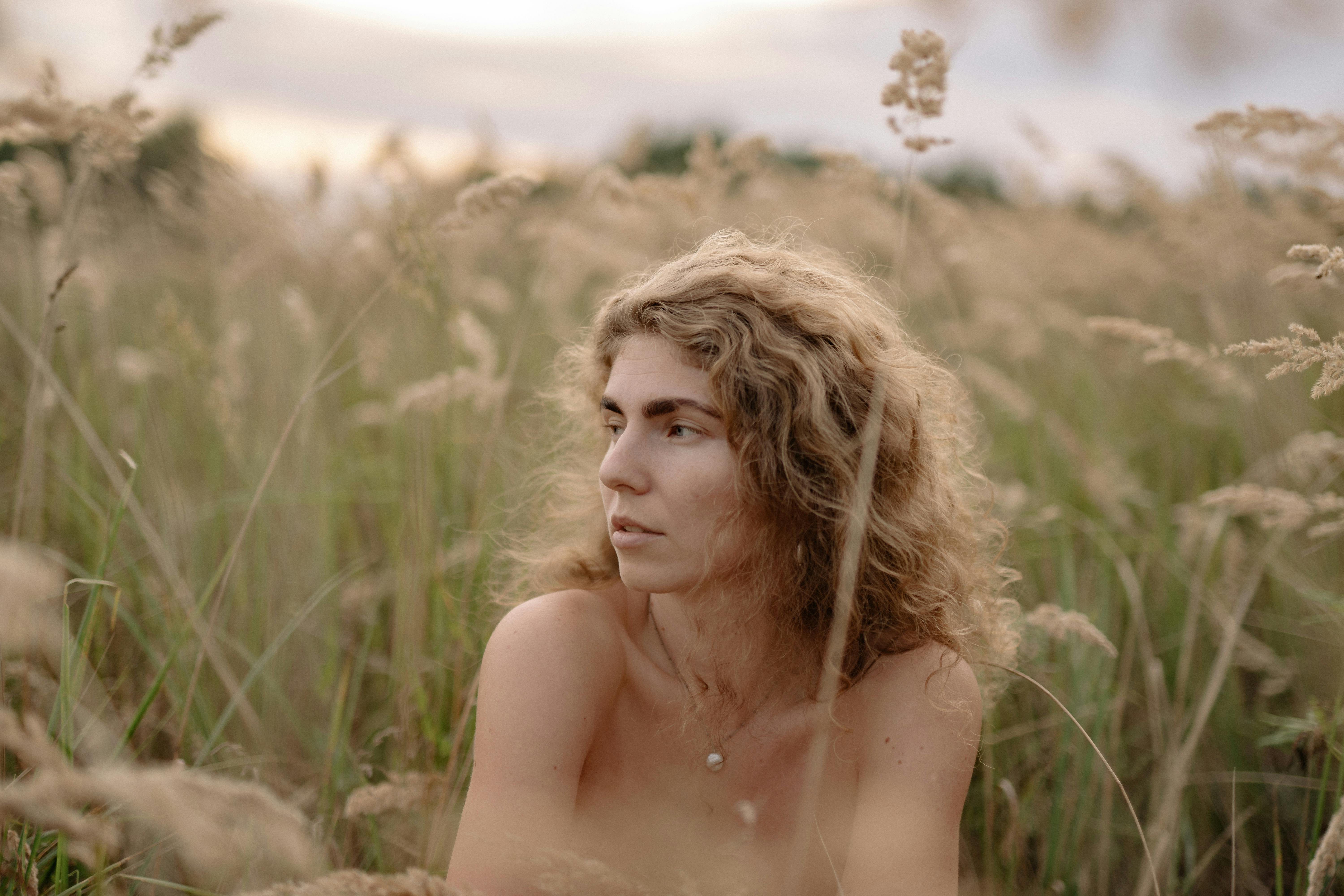 nude woman covered by grass posing on a field