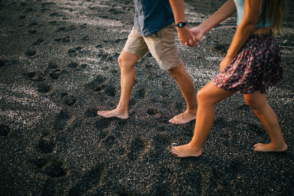 A young couple walking barefoot on a beach, holding hands