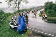 山路上，一名穿着雨衣的女子骑着摩托车在雨中前行