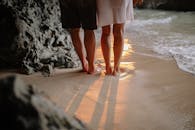 日落时分沙滩上情侣双腿剪影，凸显浪漫与宁静