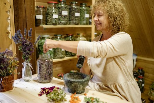 一名妇女在乡村厨房里用研钵研磨香草，架子上摆满了罐装香草