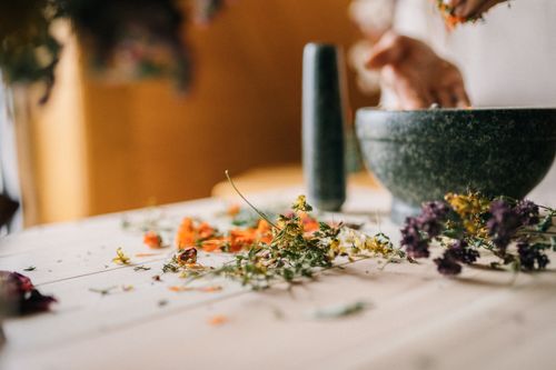 Free Close-up of dried flowers and herbs being processed in a mortar and pestle on a wooden table. Stock Photo