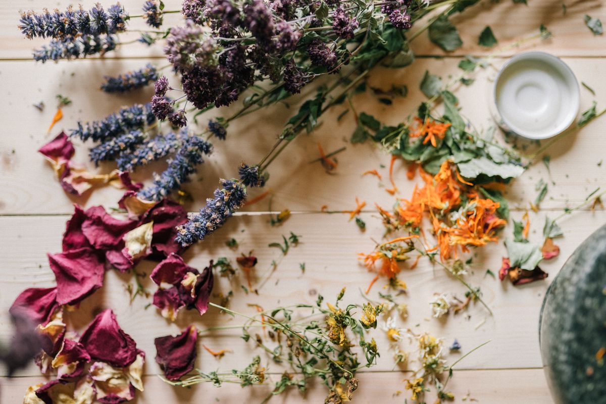 An assortment of dried lavender, rose petals, and calendula flowers scattered on a wooden table