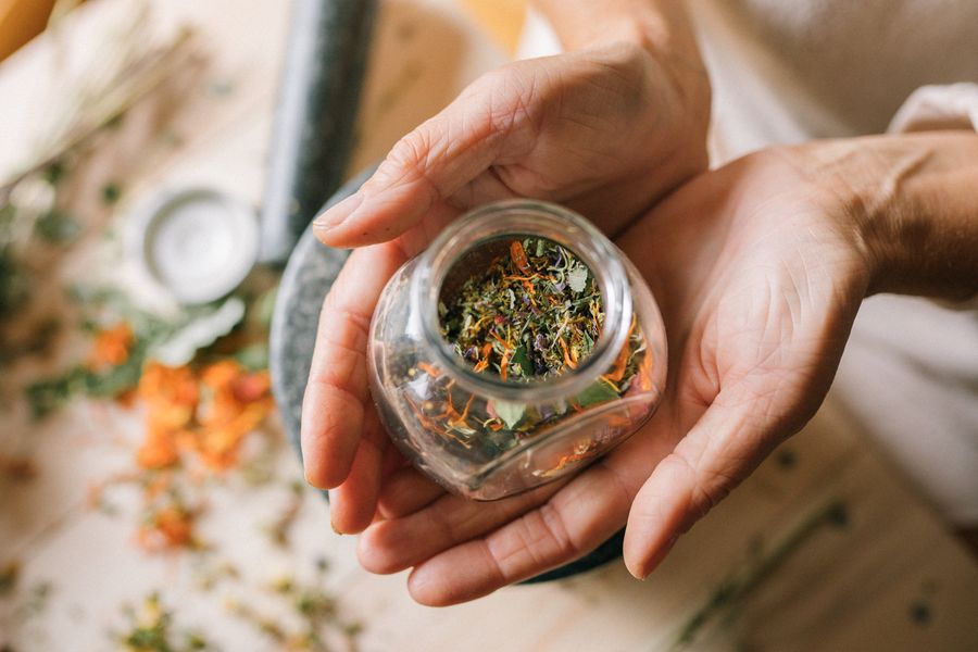 Manos sosteniendo frasco con hierbas medicinales — herbolaría