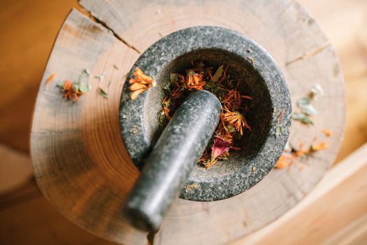 Close-up of a granite mortar and pestle grinding dried flowers on a wooden surface.