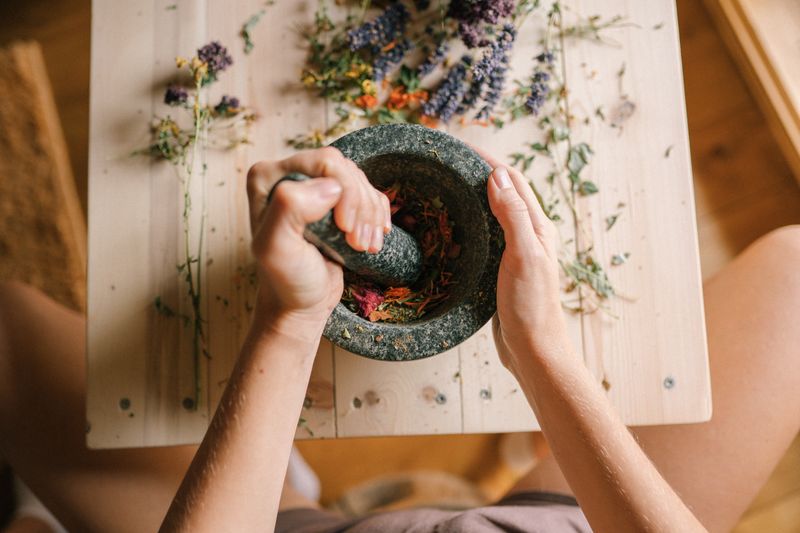 Hands grinding dried flowers with a mortar and pestle