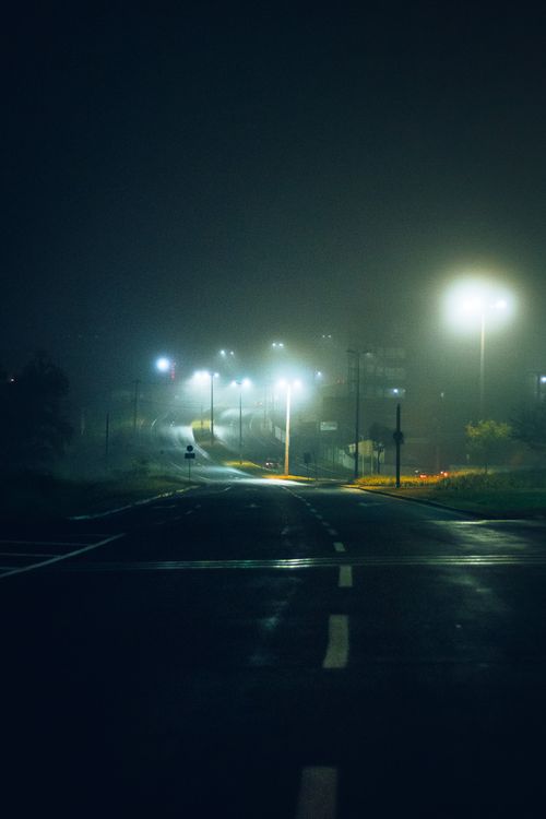 Free Eerie misty road at night illuminated by glowing streetlights, creating a moody atmosphere. Stock Photo