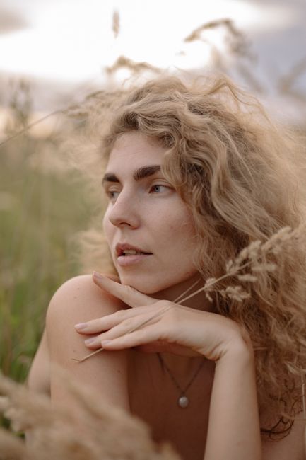 Close-up portrait of a woman with curly hair amidst dried grass, evoking a dreamy and serene mood.
