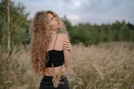 Woman in Black Spaghetti Strap Crop Top and Blue Denim Jeans Standing on Brown Grass Field