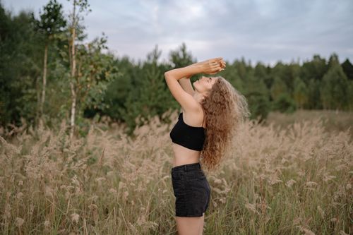 Free Side view of a carefree woman with curly hair embracing nature in a grassy field. Stock Photo