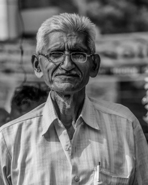Free A timeless black and white portrait of a senior man wearing eyeglasses and a striped shirt, smiling gently. Stock Photo