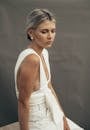 Thoughtful female with tucked back hair in white clothes wearing earrings looking down while sitting on chair on gray background