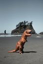 Full body of anonymous person wearing dinosaur costume while standing on sandy beach near sea with rocky cliff in distance against cloudless sky