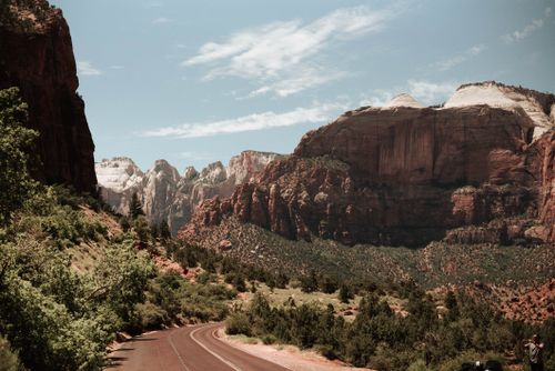Free Picturesque view of narrow curly road running among green bushes in semidesert area with rocky cliffs against cloudy sky in nature Stock Photo