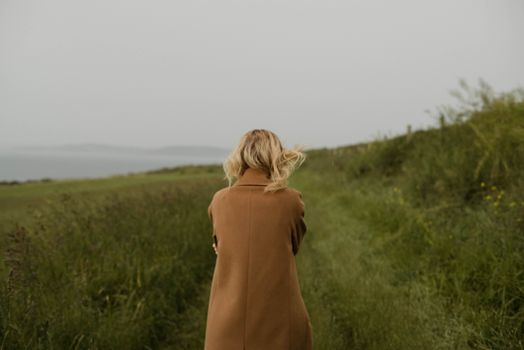 一个女人穿着外套，独自走在海边的草地上，天空阴暗