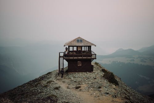 Small cabin with terrace on remote high cliff against mountain ridge in dense fog