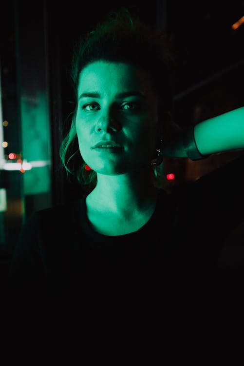 Casual female looking at camera standing in dark illuminated with green neon light