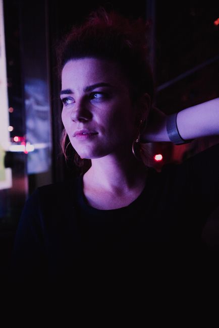 Calm young woman looking away while standing in purple neon light in dark