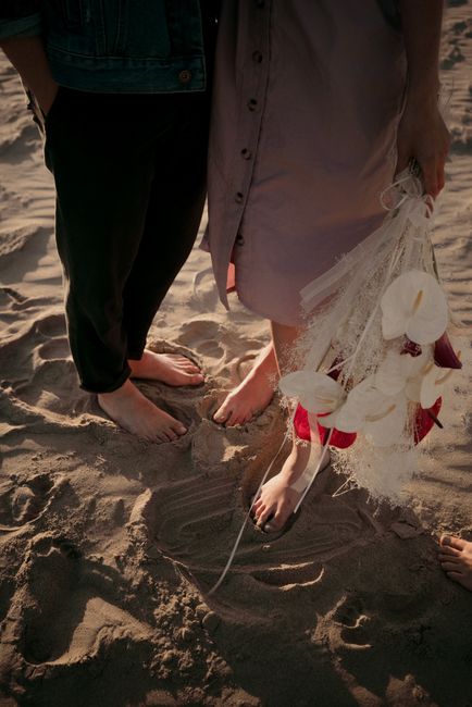 From above faceless barefoot man and woman with bouquet on sunny sand of coastline