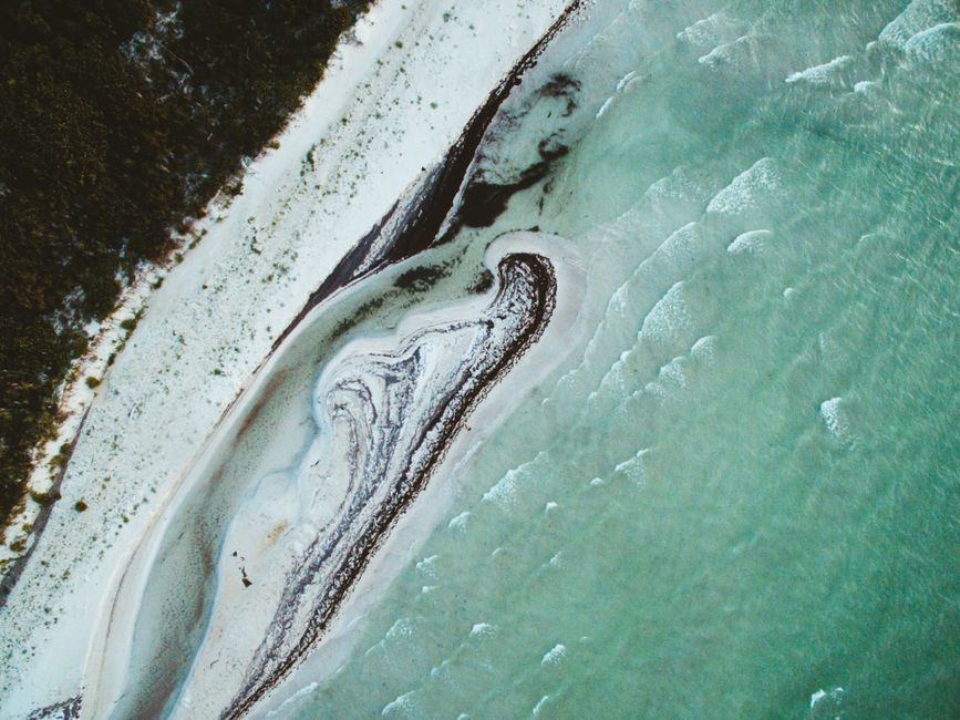 Aerial top view of turquoise water washing majestic white sandy coast with greenery