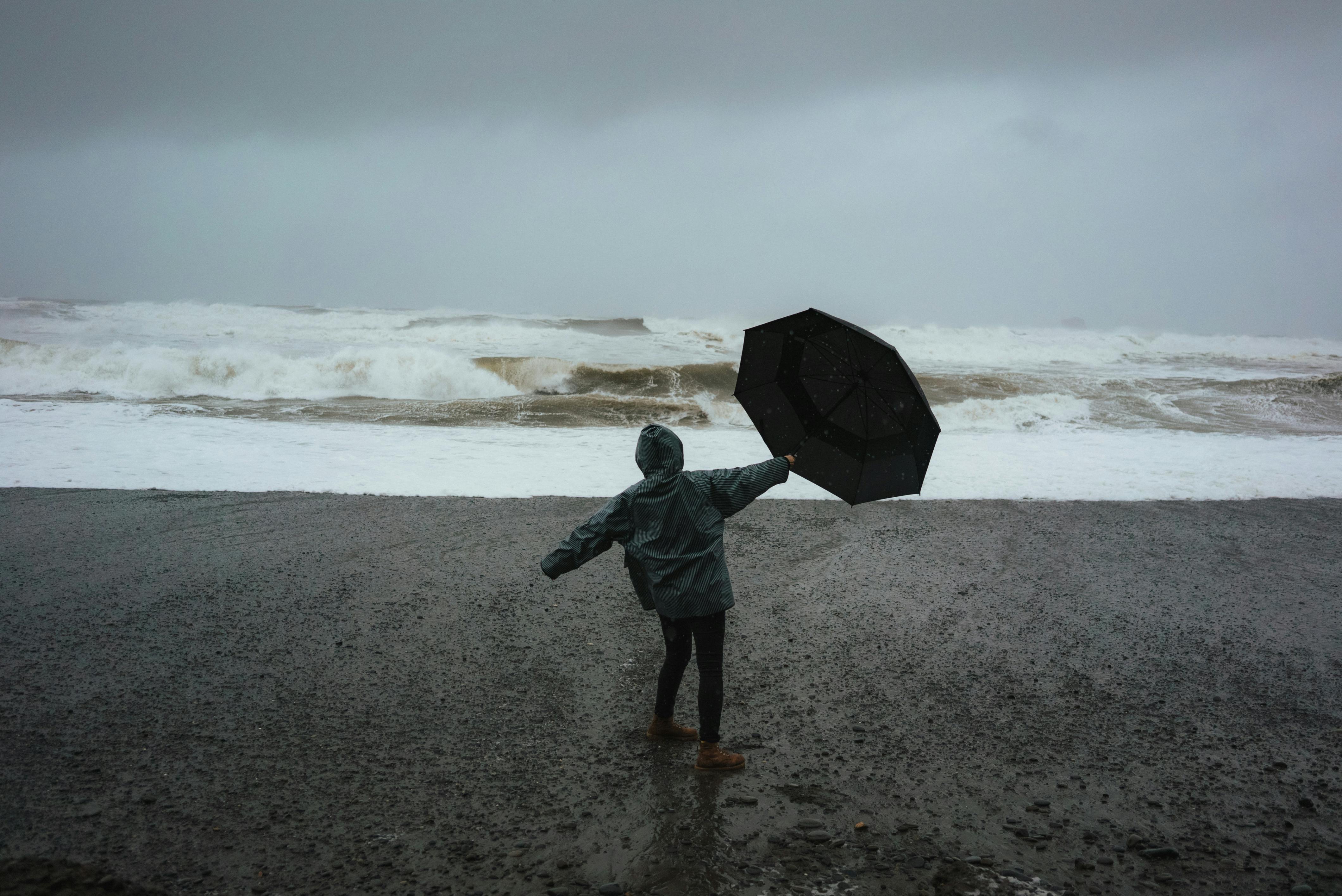 person with umbrella on shore in storm