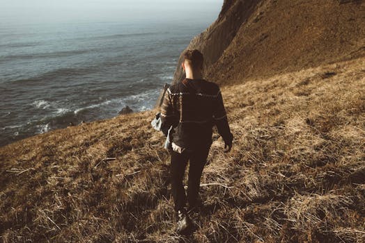 A man walks along a grassy cliffside overlooking the ocean, enjoying a serene coastal hike.