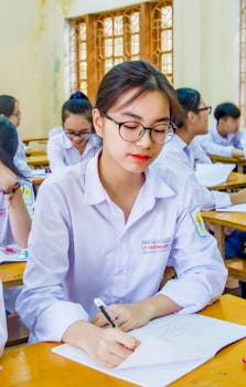 Asian girl in school uniform writing in a classroom setting, focused on studying.