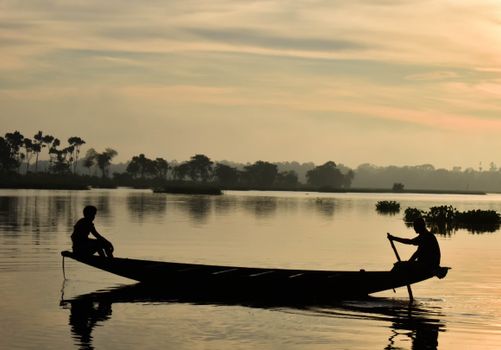 Silhouettes of two people on a boat during a tranquil lake sunset. Ideal for travel and nature themes.