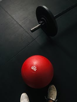 Red medicine ball and barbell on gym floor, perfect for fitness themes.