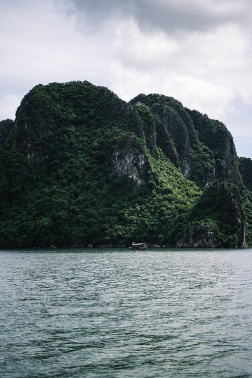 Free Lush green mountains overlooking a tranquil sea under clouded skies. Stock Photo