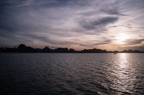 日没時の穏やかな海の近くの山のシルエット