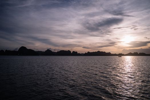 在日落天空的戏剧性背景下，下龙湾的岩石海景展现出美丽的景色