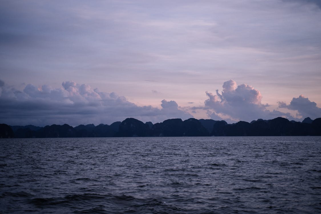 Cuerpo De Agua Cerca De La Montaña Bajo Nubes Blancas