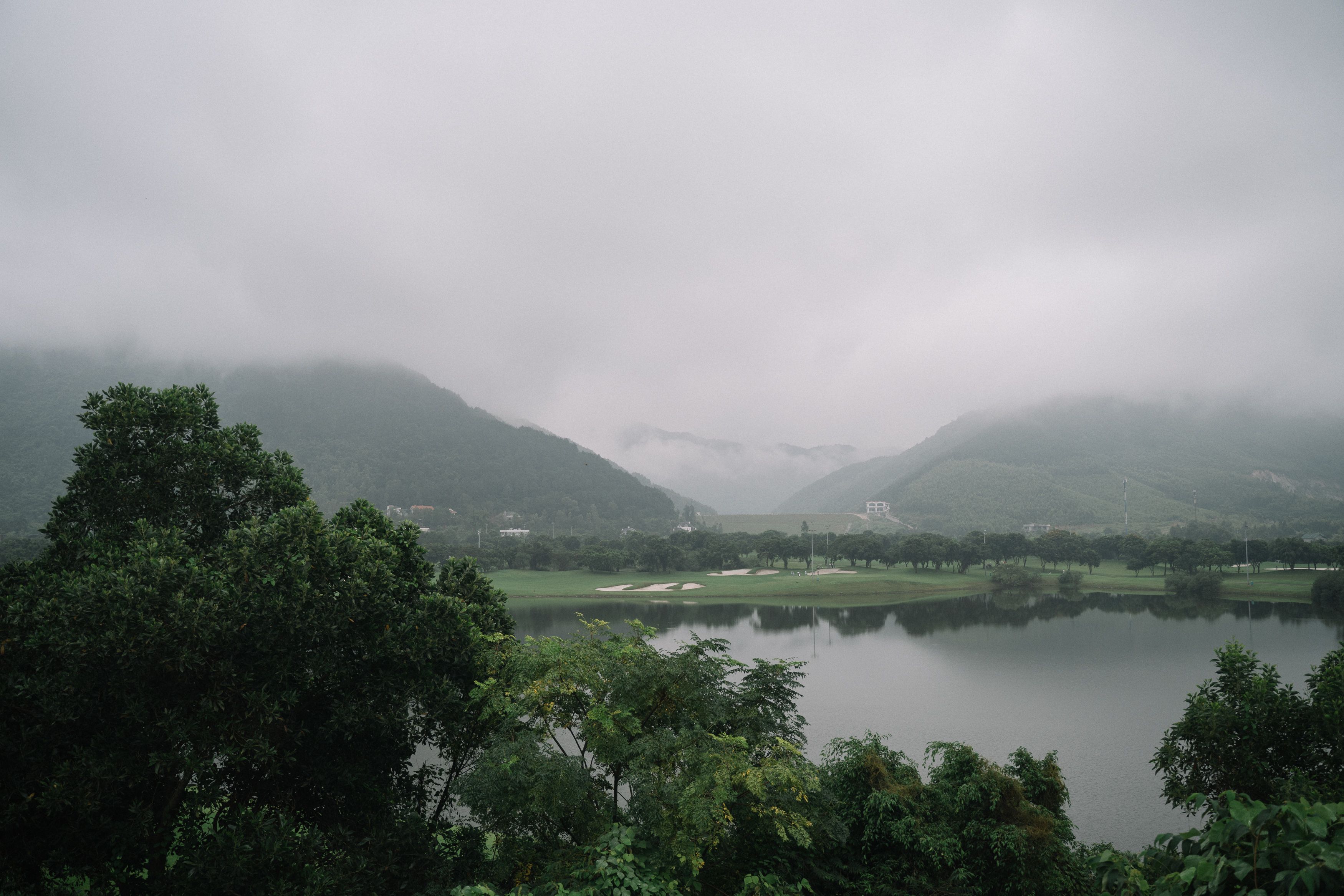 薄雾笼罩的宁静景观中，郁郁葱葱的山脉环绕着绿树成荫的湖泊